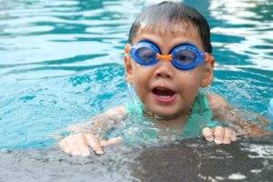 child swimming in pool with goggles